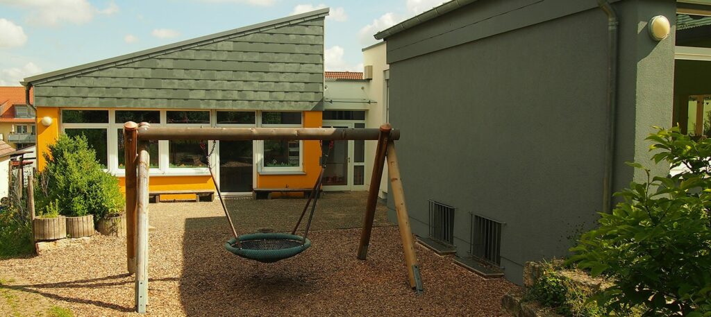 Nestschaukel vor gelbem Kindergartenhaus