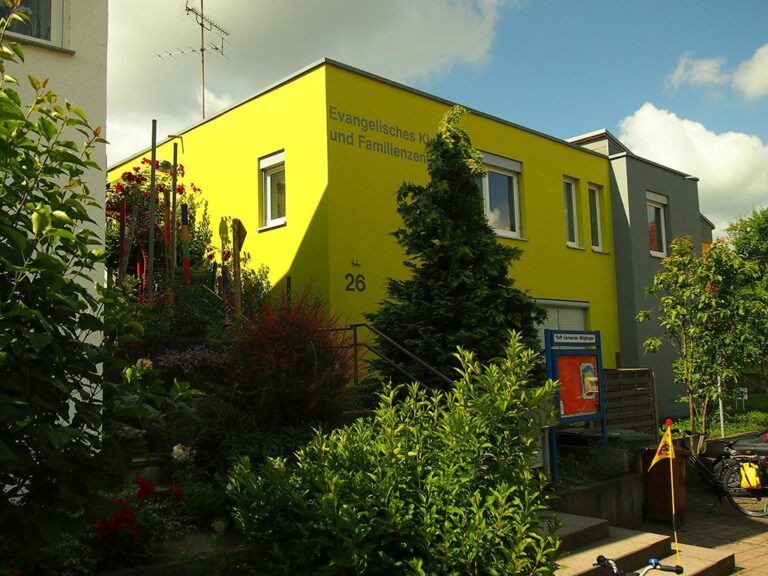 Knallgelbes Gemeindehaus, blühende Gartenpflanzen.